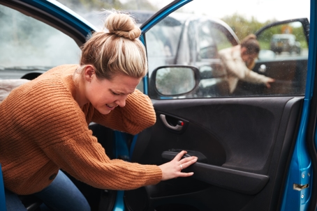 Two women getting out of their cars holding their heads after being involved in a car wreck.